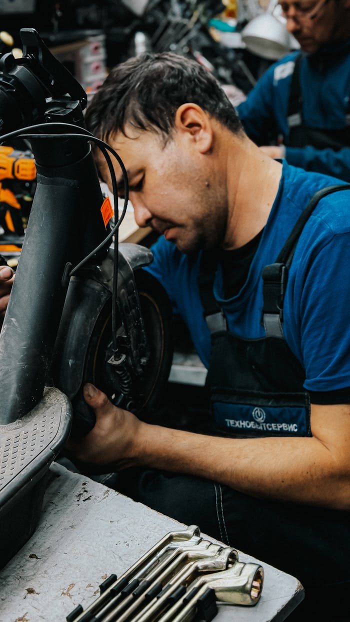 heros-img Mechanic focused on repairing an electric scooter in a busy workshop environment.
